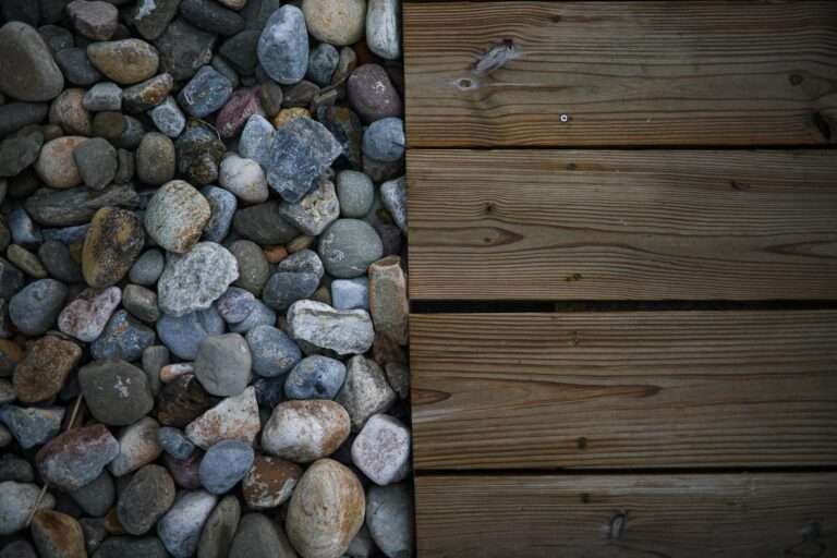 A top-down view showing a clear divide between smooth, multicolored river rocks on the left and light brown wooden planks arranged horizontally on the right.